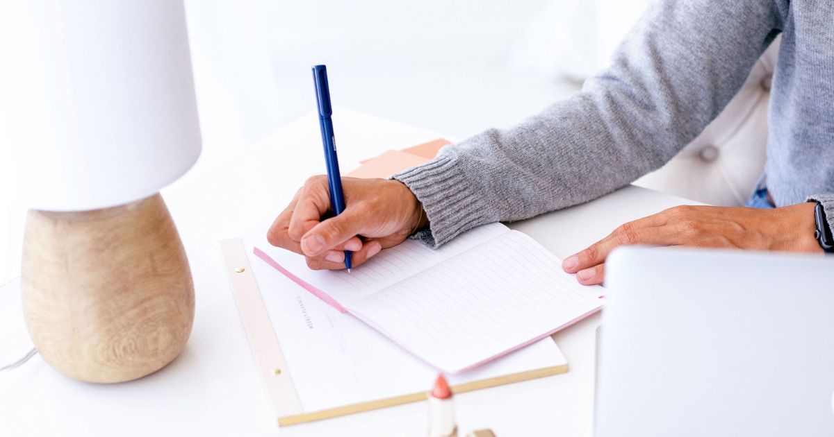 Une femme écrit dans un carnet sa recherche de mots-clés pour son auto-entreprise